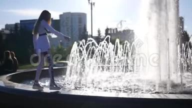 一个快乐美丽的模特女孩沿着喷泉的边缘走着，高兴着，举起双手，经过鸽子。 高清高清